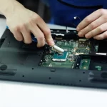 technician-clearing-circuit-board-disassembled-laptop